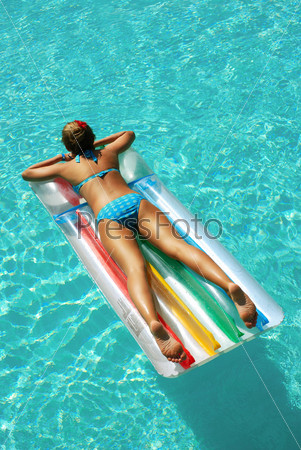 Девушка плавает в бассейне на надувном матрасе