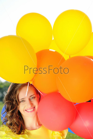 Woman holding balloons against sun and sky