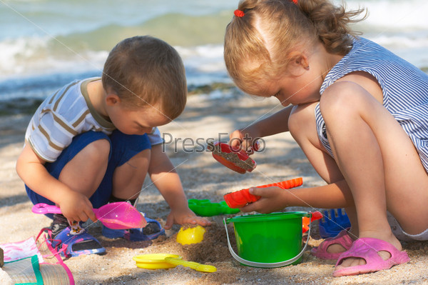 Small girl and boy play with sand near sea