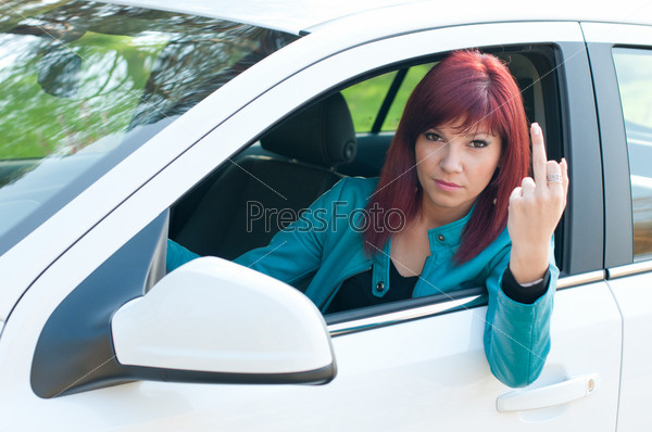 Negative female driver sitting behind the wheel and showing her middle finger