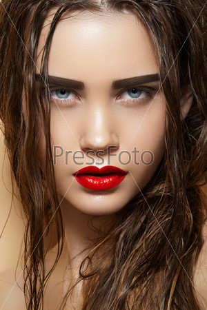Hot young woman model with sexy bright red lips makeup, strong eyebrows, clean shiny skin and wet hairstyle. Beautiful fashion portrait of glamour female face