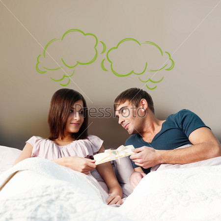Closeup portrait of adult couple lying on their bed at their apartment and man giving a greeting card to his girlfriend. Blank balloon at the top of the photo for your text. Planning future concept