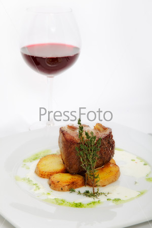 roast meat with potatoes on white plate with glass of wine