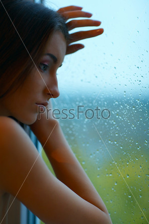 beautiful sad woman stands near the window in rainy day