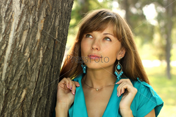 The beautiful girl in a turquoise dress costs at a tree and looks upwards
