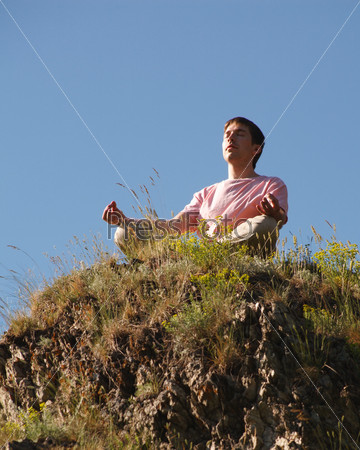 Image of relaxed young man sitting on cliff and meditating outside