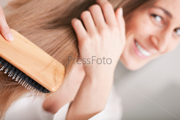 Young woman in pyjama brushing her long dark-blond hair after getting up in the morning
