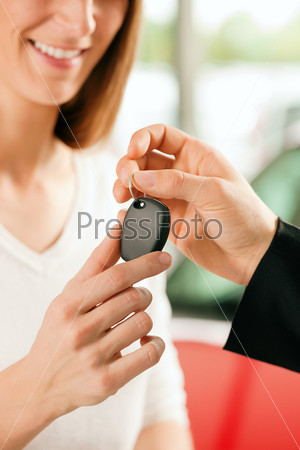 Woman at a car dealership buying an auto, the sales rep giving her the key, macro shot with focus on hands and key