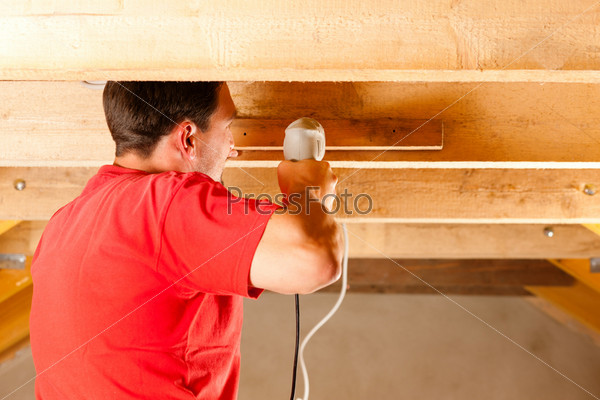 Carpenter or construction worker with hand drill working in the roof framework inside a house