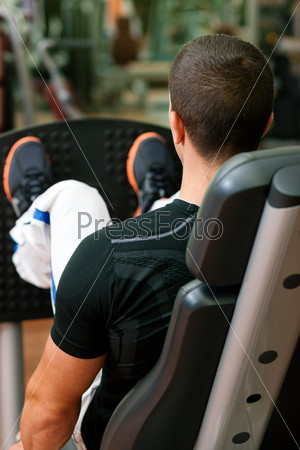 Man doing fitness training on leg press with weights in a gym