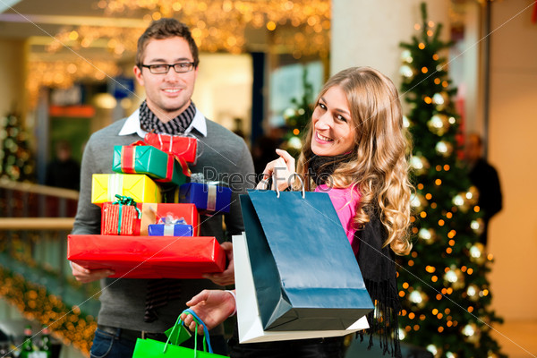 Couple - Caucasian man and woman - with Christmas presents, gifts and shopping bags - in a mall in front of a Christmas tree