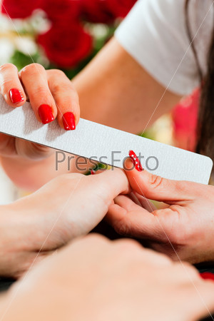 Woman in a nail salon receiving a manicure by a beautician, lots of roses in the background