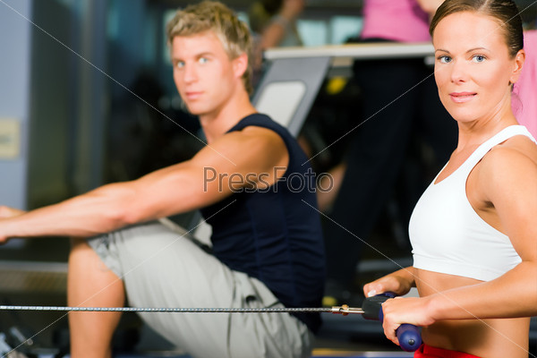 Two people working out in a gym using a rowing machine