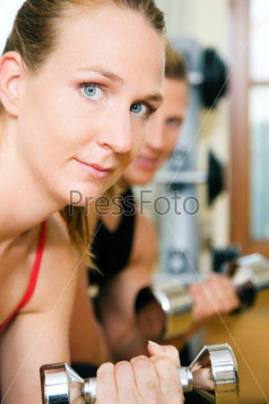 Couple (male / female) having a workout with dumbbells in a gym (woman in front)