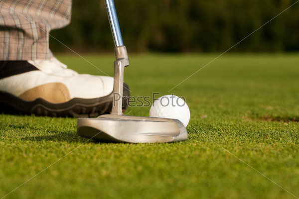 Golf player attempting the tee stroke in the teeing area (only legs of player to be seen, focus on ball)