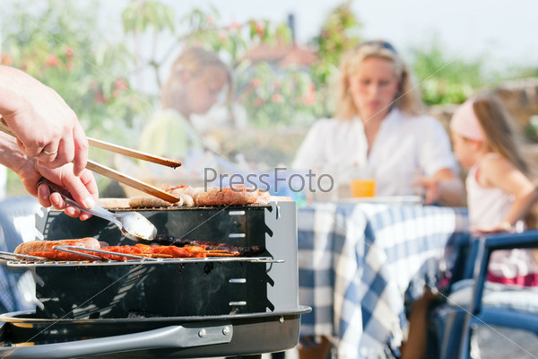 Family having a barbecue in the garden - focus on cooking in the foreground
