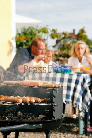 Family having a barbecue in the garden, eating (focus on barbeque grill!)