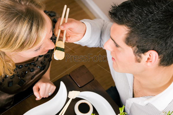 Couple feeding each other with sushi for dinner, romantic setting, presumably this is an advanced date; shallow focus on eyes