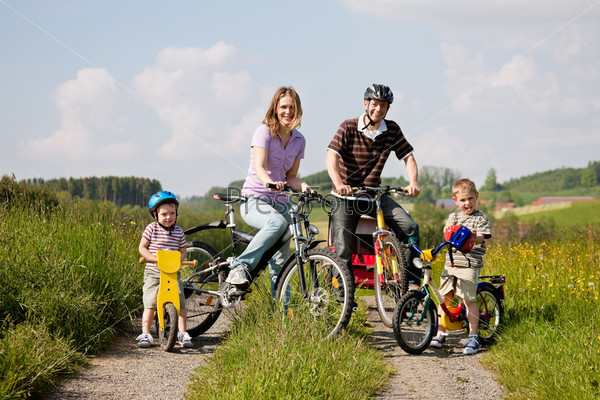 Family with two children having a weekend excursion on their bikes on a summer day in beautiful landscape, for safety and protection they are wearing helmets