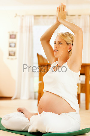 Pregnant woman meditating doing pregnancy yoga sitting on the floor in her home, stock photo
