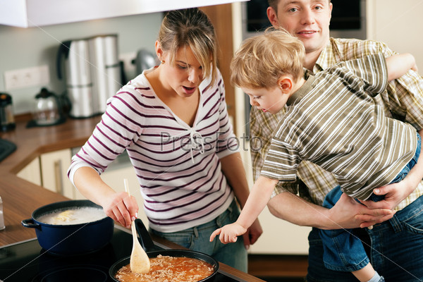 Family cooking in their kitchen - mother stirring some spaghetti sauce, son and father yearning for it