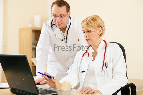 Two doctors - male and female - discussing test reports that show on their laptop screen