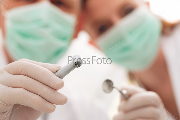 dental treatment with dentist and dental assistant bowing over the patient as seen from patient\'s perspective. They have drills and angled mirrors, focus on tools