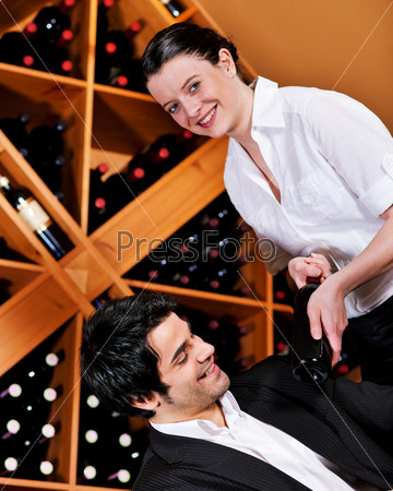 Waitress in a wine bar or restaurant offers a bottle of red wine to a young mediterranean looking man