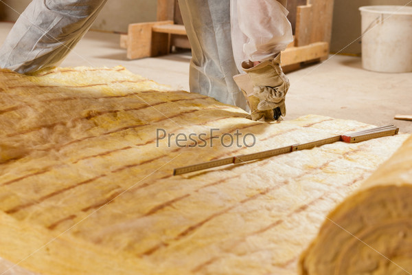 Man - only hand to be seen - cutting some glass wool as material for thermal insulation of a new building