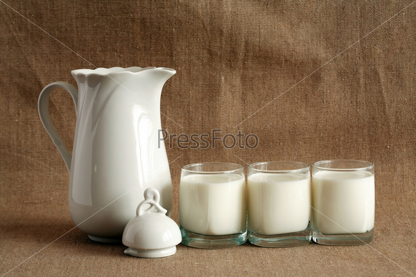 Three glasses full of milk near open pitcher on canvas background
