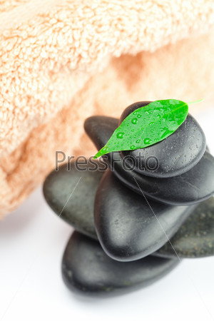 black spa stones with green leaf and a drop of water on the towel