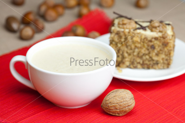cup of cappuccino, a piece of cake with nuts on a plate lying on a red background