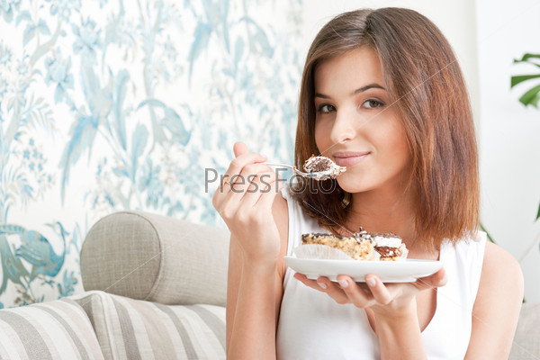Smiling brunette woman eating some cake in the living room in her apartment