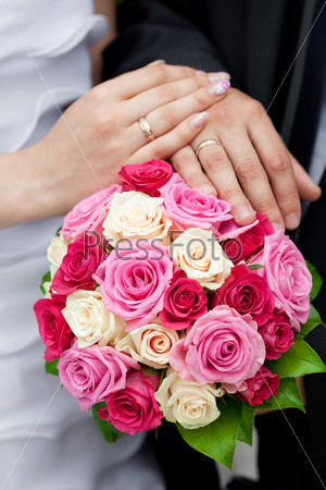 the hands of the bride and groom lying on the bridal\
bouquet