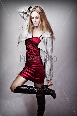 Fashion portrait of young sexy woman in red dress, gray leather jackets and black long boots on high heel
