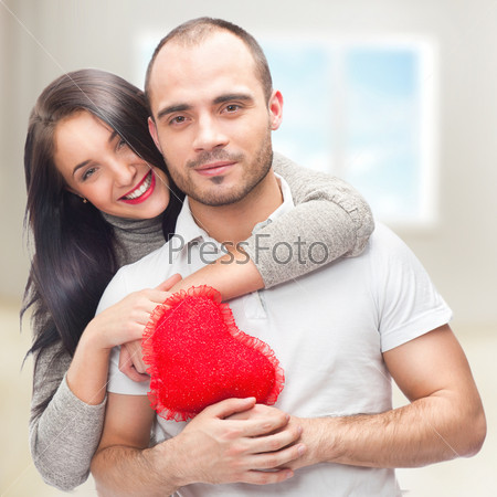 Portrait of young couple with red heart standing at their home and embracing. They are really happy to be together