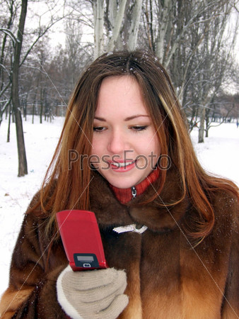 The girl in the winter in park with phone in a hand