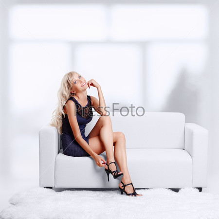 full-length portrait of beautiful young blond woman on couch checking court shoe fastener