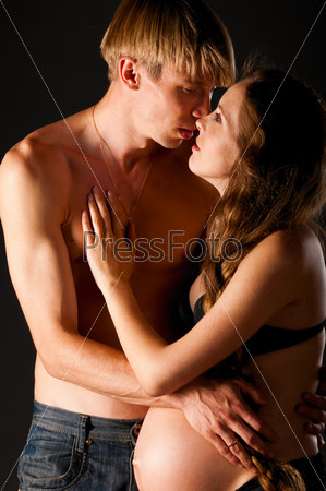 Pregnant woman is kissing with man on black background