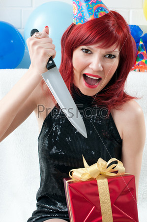 Emotional red-haired party woman screaming and opening a gift box with a kitchen knife
