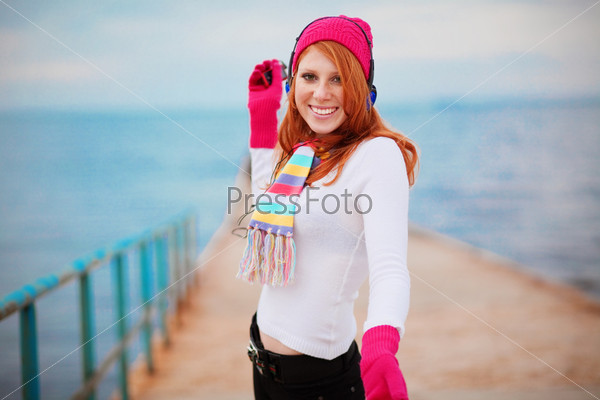 Fashion teenage girl wearing winter clothing is listening to music near the sea