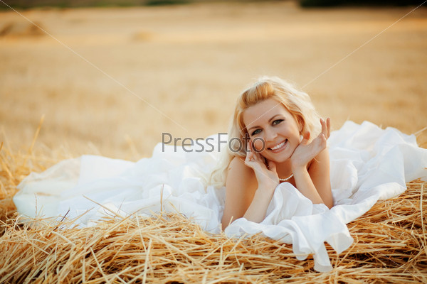 Beautiful bride relaxing in hay stack at her wedding day