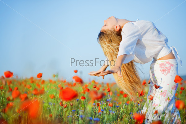Bending blond young woman in field of flowers in summer