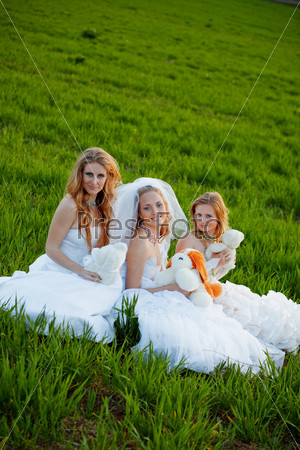 Three happy brides with teddy bears posing on fresh green grass