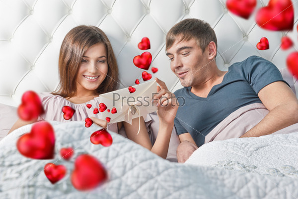 Young happy couple presenting gift in bed