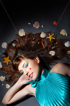 Beautiful model stylized as mermaid posing on gray studio background