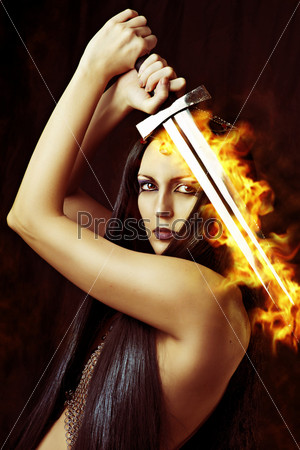 Young sexy woman warrior holding fire sword in hands with long healthy black hair.