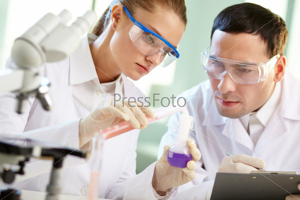 Portrait of two chemists combining different liquids in tubes, stock photo