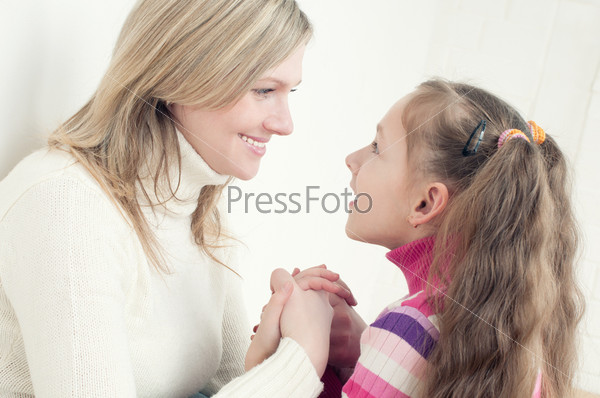 Happy young mother and her little daughter looking at each other and holding each other by the hands