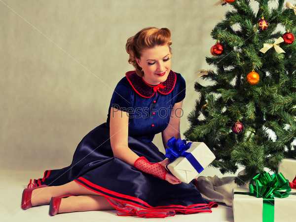Woman sitting near a Christmas tree with gift in hand
